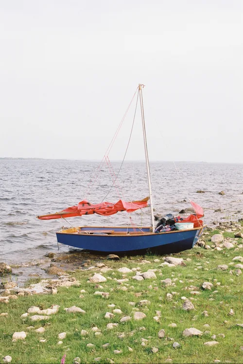 A small blue sailing dinghy pulled up on the rocky, grassy shore of the Shannon.